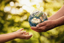 A person handing a rock that looks like Earth to a kid.